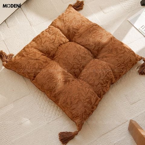 Bối cảnh đặt trên sàn nhà cạnh ghế tựa gối tựa sofa Tasselo màu nâu hoa văn dệt nổi có tua rua viền.
