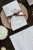 Thiệp cưới giấy cao cấp tông trắng kem, họa tiết hoa mẫu đơn, ruy băng nâu sang trọng đặt trên nền gỗ