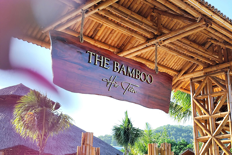 Một cổng chào bằng tre kiểu dáng có mái che với 2 cột 2 bên và bảng gỗ treo ở giữa The Bamboo Hà Tiên 